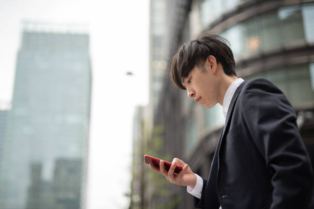 Young businessman watching smart phone Portrait of young Asian cool-attitude businessman on street low angle street japan stock pictures, royalty-free photos & images