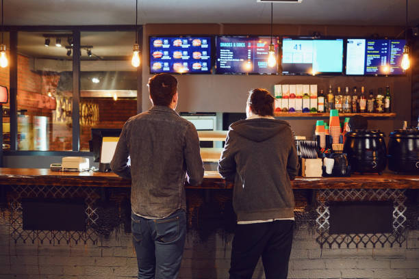 Two men choose food in a fast food restaurant. Rear view. Two men choose food in a fast food restaurant. Bar snack concept . fast food stock pictures, royalty-free photos & images