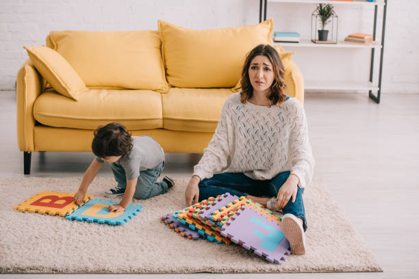 istock sad mother and son playing with alphabet puzzle mat on carpet 1151575825