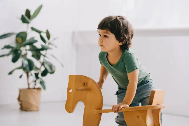 cute child with wooden rocking horse in living room