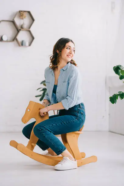 Joyful woman in jeans sitting on rocking horse and looking away