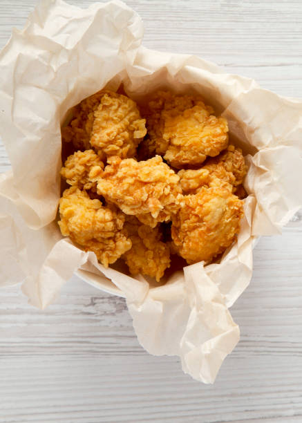 istock Fried chicken bites in a paper box over white wooden surface, top view. Flat lay, overhead, from above. Close-up. 1151584021