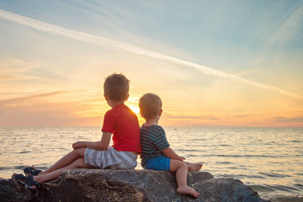 Two boys sitting on the rock at the beach watching beautiful sunset, South Australia