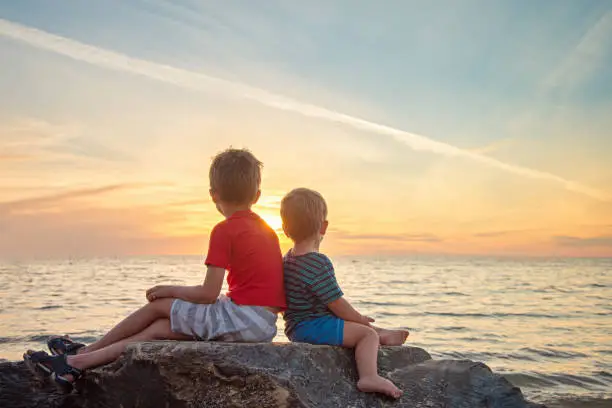 Photo of Two boys sitting on the rock at the beach at sunset