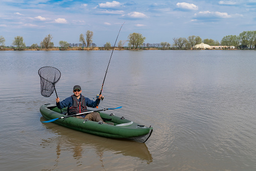 Kayak fishing at lake. Fisherman on inflatable boat with fishing tackle.