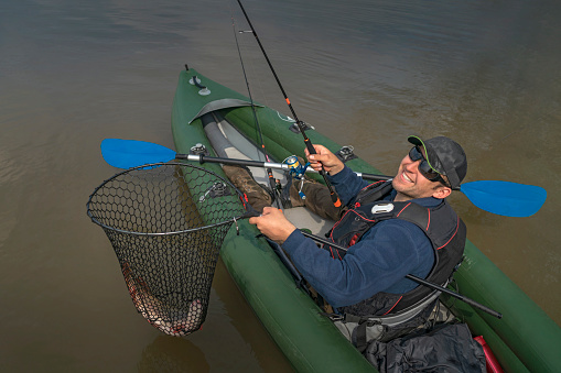 Kayak fishing at lake. Fisherman caught pike fish on inflatable boat with fishing tackle.