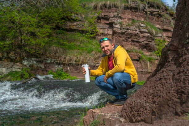 istock Man drinking coffee from white thermos near mountain river 1151585895