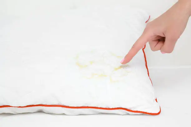 Photo of Woman's hand finger pointing to saliva stain on white pillow. Cleaning problem and solution concept. Closeup.