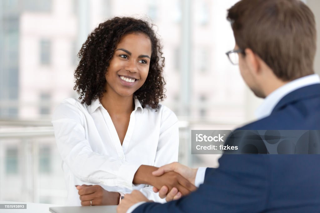 Smiling african hr manager handshake hire candidate at job interview Smiling african female hr manager handshake hire male candidate at job interview make good first impression, happy mixed race client shake hand of bank broker, respect, business agreement concept Customer Stock Photo