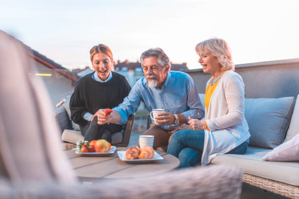 Family enjoying snacks at building terrace Family enjoying snacks at building terrace during sunset. Senior parents sitting with young daughter on sofa. They are in casuals. 1354 stock pictures, royalty-free photos & images