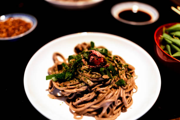 plato tradicional japonés con fondo de mesa de madera lacada en negro y plato vegetal con fideos soba, algas y umebosho con cebolla verde - 13576 fotografías e imágenes de stock