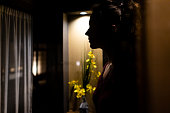 夜の窓辺に、黄色い生け花のデコレーションとカーテンで女性が映る伝統的な日本家屋または旅館