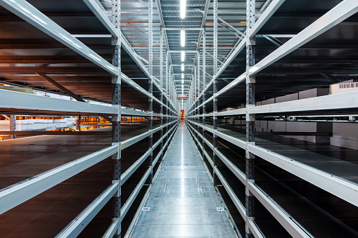 Interior of the new and modern warehouse space in a well lit large room. Rows of empty shelvings and with boxes
