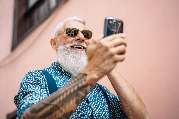 Happy senior man messaging on mobile smartphone outdoor - Bearded hipster fashion male having fun with new technology apps for social media - Concept of tech and elderly fashion people mensajería de hombre senior feliz en el teléfono inteligente móvil al aire libre-hombre de moda hipster con barba que se divierten con nuevas aplicaciones tecnológicas para las redes sociales-concepto de la tecnología y la gente de moda de edad