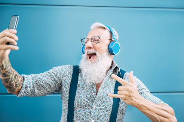 starszy szalony człowiek biorąc własny film podczas słuchania muzyki ze słuchawkami - hipster facet zabawy za pomocą aplikacji mobilnych smartphone playlist - szczęście, technologia i starszych ludzi stylu życia koncepcji - headphones music mobile phone tattoo zdjęcia i obrazy z banku zdjęć