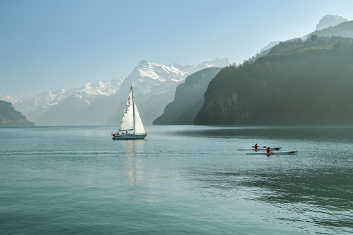Brunnen, Switzerland - March 30, 2019: Sailing boat chasing couple in kayaks on Lake Luzern near Brunnen in Switzerland during sunny spring day 2019