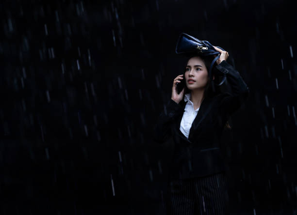 a mulher asiática está usando sacos rainproof, chuva está caindo. she está falando no telefone - wet dress rain clothing - fotografias e filmes do acervo