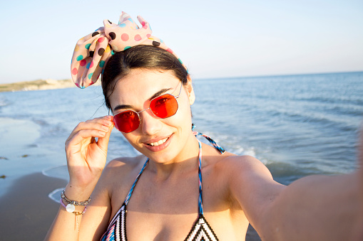 Beautiful smiling woman is taking selfie on the beach. Summer concept.