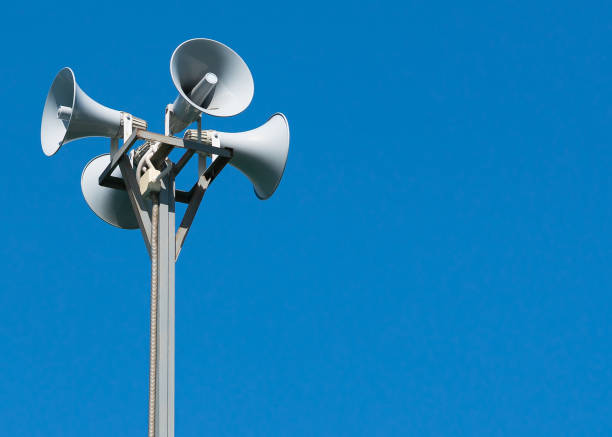 Four loudspeakers attached to a rack on a blue background. A tall column with four gray loudspeakers in a circle against a clean blue sky. Hazard warning system. The possibility of placing your test or image. public address system stock pictures, royalty-free photos & images