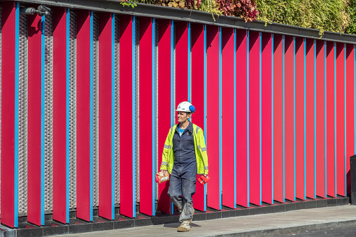 London, UK - 18 May, 2019 - A male construction worker walking past a vibrant patterned wall around Camden