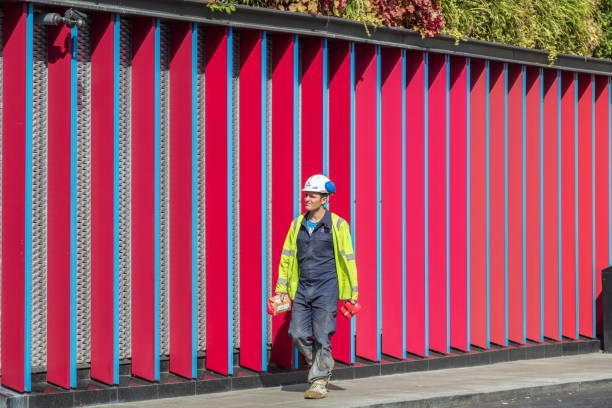 A male construction worker walking past a vibrant patterned wall around Camden London, UK - 18 May, 2019 - A male construction worker walking past a vibrant patterned wall around Camden construction lunch break stock pictures, royalty-free photos & images