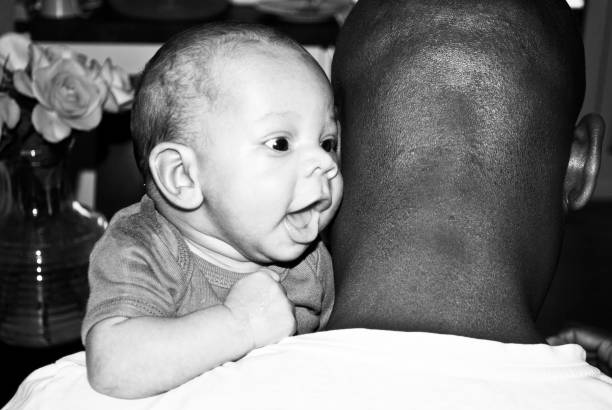 Black and white shot of happy parents looking at their baby boy lying on blanket at home