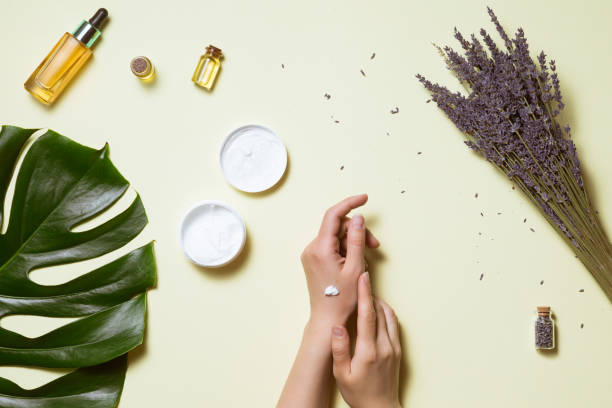 top view and flat lay of woman holding cream on hands over white table with cosmetic products - avocado oil, cream and bamboo - leaf epidermis imagens e fotografias de stock