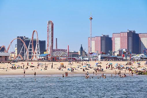 New York, USA - July 02, 2018: Crowded Coney Island beach and amusement parks seen from the pier on a sunny day.