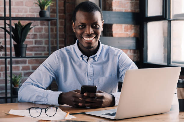 istock African guy working in cafe holding smartphone in hands and looking at camera with smile 1151641797