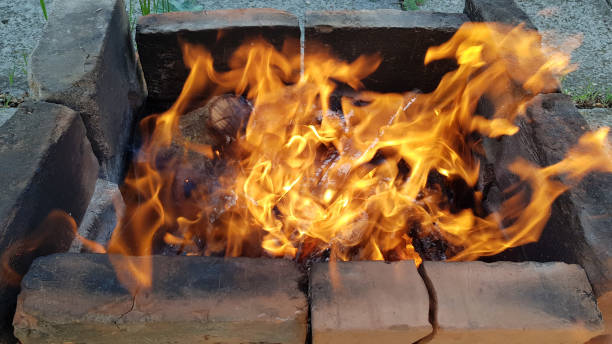 istock Bonfire with bright orange flame in old firewood brazier made from burnt smoky bricks into ground. Fire is flaming in windy weather. Blurry blazing campfire structure closeup. 1151644004