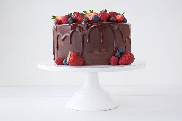 pastel con chocolate, decorado con varias bayas en una mesa blanca. - tarta postre fotografías e imágenes de stock