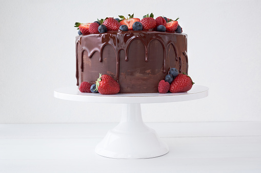 Cake with chocolate, decorated with various berries on a white table. Strawberries, blueberries, raspberries.
