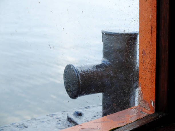 Iron bollard through the dirty wet window of the small boat with water on the background. stock photo