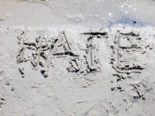 Word Hate written on the sand next to the water, slowly eroded by waves. The concept of forgiveness. stock photo