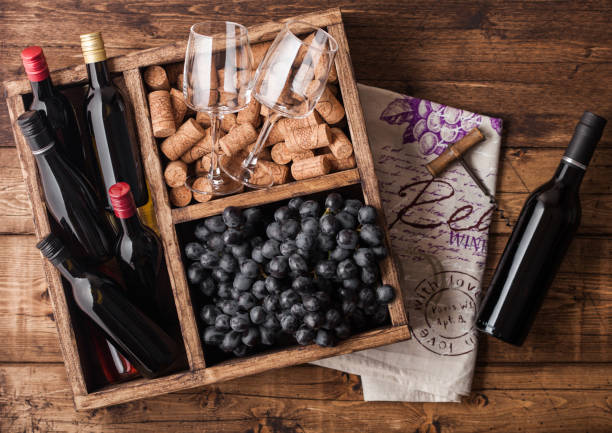 istock Mini bottles of red wine and empty glasses with dark grapes with corks and opener inside vintage wooden box on grunge wooden background with linen towel. Top view 1151662761