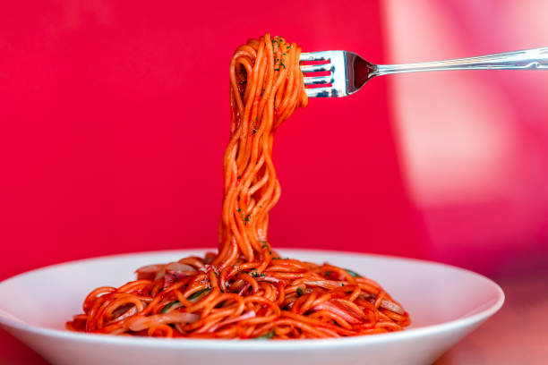 nahaufnahme von roten sauce italienischen nudeln mit gabel hält basilikum auf weißem teller in italien restaurant oder studio - vibrant color tomato vegetable pasta stock-fotos und bilder
