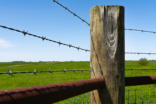 Wooden post and barbed wire with prairie and blue skies in the background.