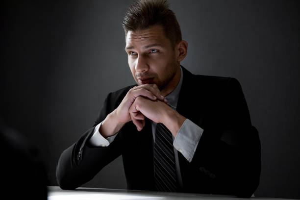istock Serious detective with hands on chin in dark interrogation room 1151683319