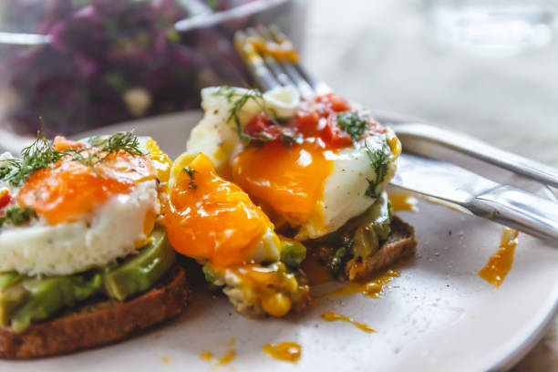 istock Breakfast served of two toasts with avocado, fried eggs with vegetables and herbs on a rustic tablecloth background. View from above. Healthy and nutritious food concept. 1151683621