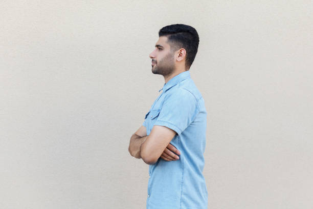 profile side view portrait of serious calm handsome young bearded man in blue shirt standing, crossed arms and looking forward. - wall profile imagens e fotografias de stock
