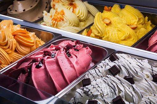 Italian gelato of various flavors (vanilla, chocolate, raspberry, strawberry, pistachio, lemon, orange, yogurt...) in ice cream parlor.