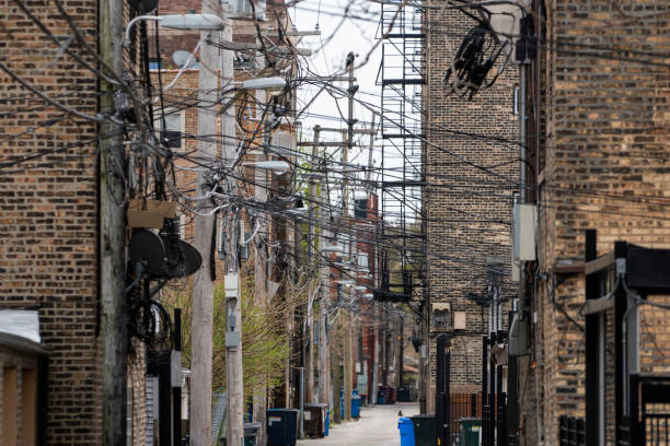 Alley with jumble of power lines and fire escapes An alleyway in daylight  with many utility poles, power lines, and street lights. seedy alley stock pictures, royalty-free photos & images