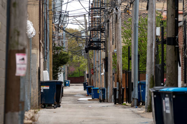 Alley with power lines and fire escape An alleyway in daylight. Dumpsters line the street, with some trash strewn about, and a park with brick wall is at the end. seedy alley stock pictures, royalty-free photos & images