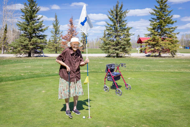 femme caucasienne âgée debout sur putting green tenant le drapeau - sports flag golf individual sports sports and fitness photos et images de collection