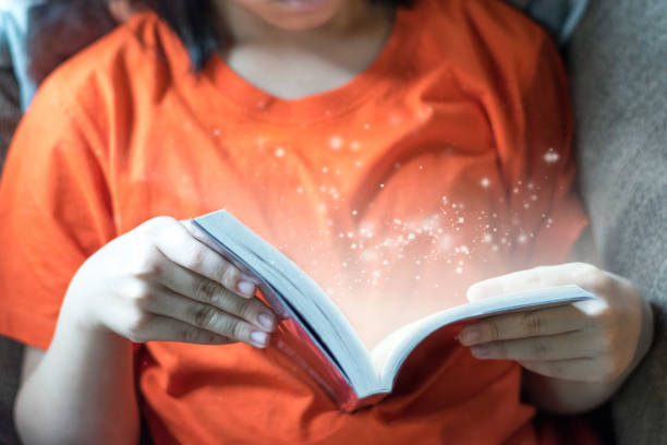 conceito da instrução da leitura. a menina da criança de ásia leu um livro adulto novo do fiction com efeito da luz da faísca. - magic hour - fotografias e filmes do acervo