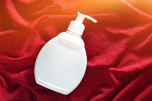 White plastic bottle of cream on a red silk background