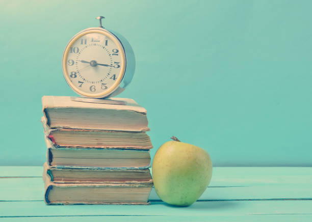istock Alarm clock on stack of old books, apple on a blue background. School concept, education. 1151731056