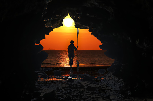 Kayaking in the cave, Asian girls holding the paddle stands in front of a cave by the sea at sunset background.