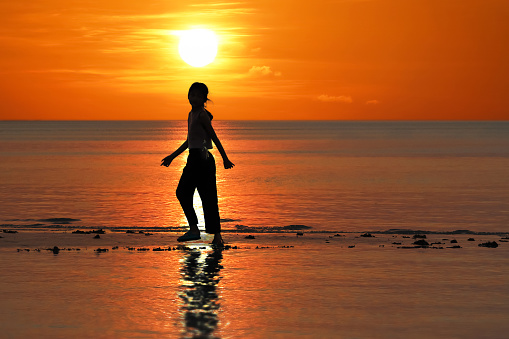 Silhouette of single Asian girl enjoying herself during sunset on the beach red sky background.