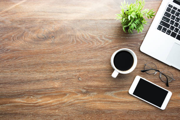 Wood desk table with smartphone with blank mock up screen, laptop computer and up of coffee with sun light in the morning. Top view with copy space, flat lay. Wood desk table with smartphone with blank mock up screen, laptop computer and up of coffee with sun light in the morning. Top view with copy space, flat lay. wooden desk stock pictures, royalty-free photos & images